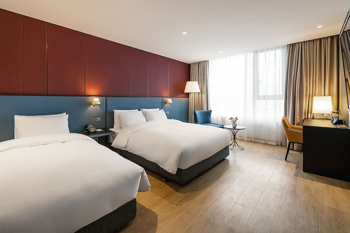 A hotel room with two beds, a desk, a chair, and a small table.