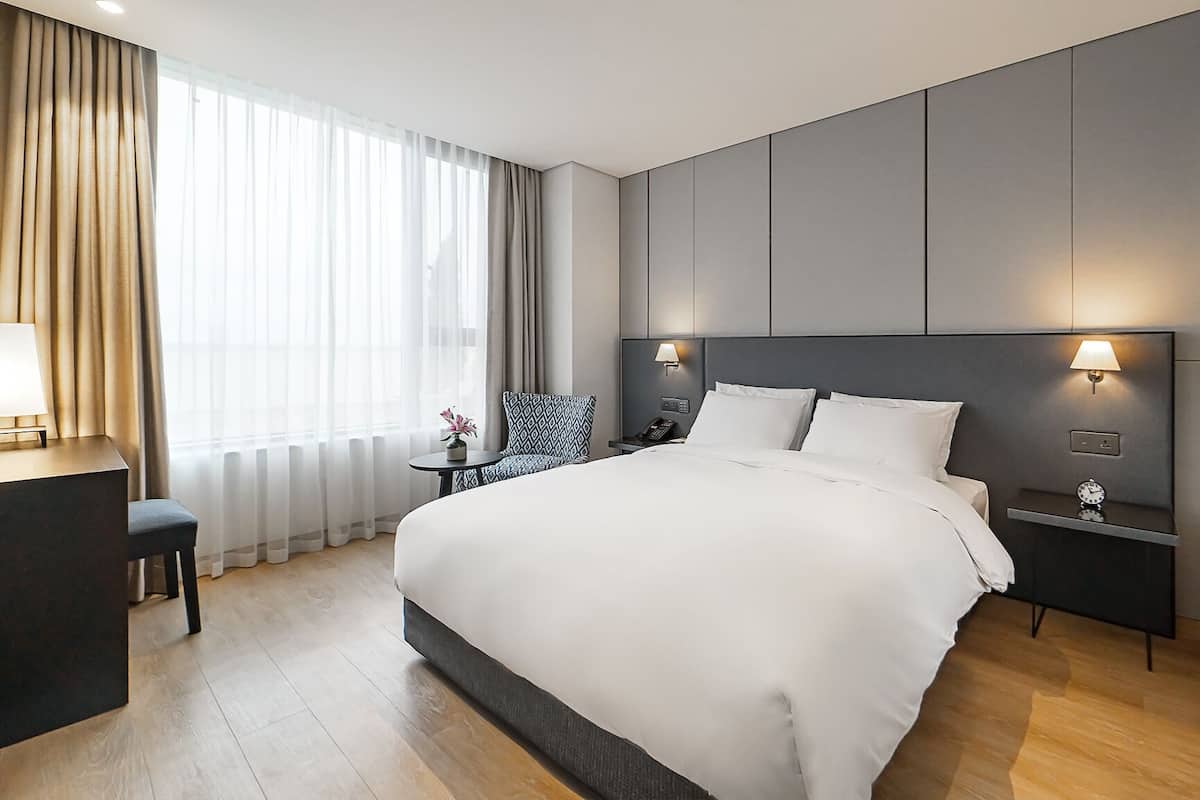 A modern hotel room with a large bed, bedside tables with lamps, a desk, and a chair.