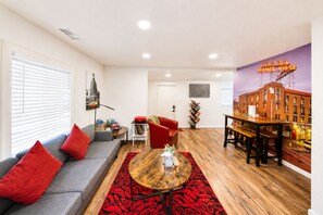 Una sala de estar moderna con un sofá, cojines rojos, una mesita de centro, una estantería y un mural en la pared.