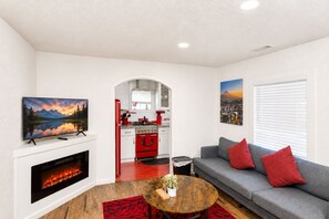 A living room with a fireplace, a sofa, a coffee table, and a kitchen in the background.