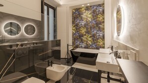 A modern bathroom with a black and white color scheme, a large mirror, a freestanding bathtub, and a wall with a tropical leaf pattern. - Cavour 83 Prestige House (Florence)