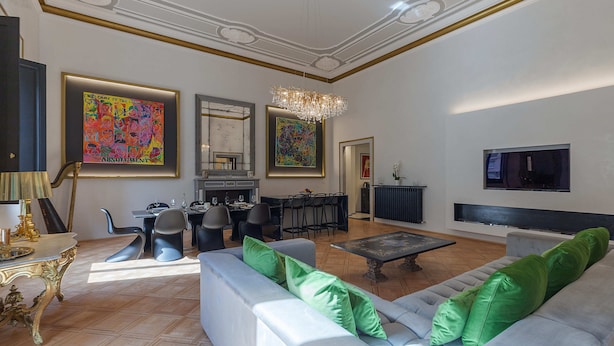 A spacious living room with a grey sofa, green cushions, a chandelier, and artwork on the walls. - Cavour 83 Prestige House (Florence)