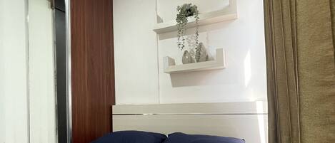 Habitación de hotel con cama, espejo, armario de madera y estante con planta.