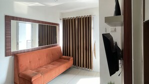 Ein modernes Wohnzimmer mit einer Couch, einem flachbildfernseher an der Wand und einem großen Fenster mit Vorhängen.
