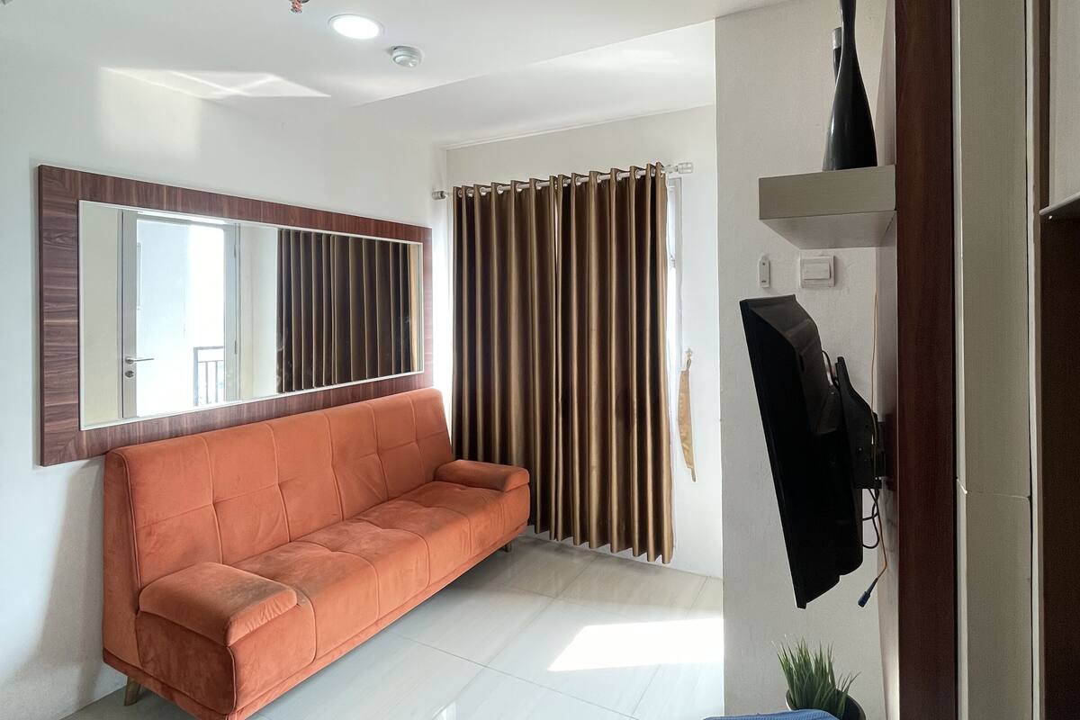Ein modernes Wohnzimmer mit einer Couch, einem flachbildfernseher an der Wand und einem großen Fenster mit Vorhängen.