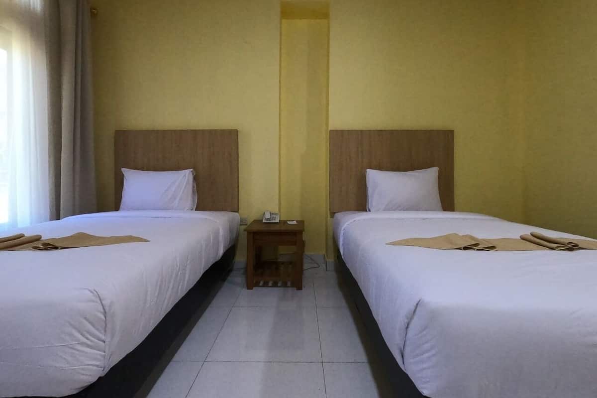 A hotel room with two single beds, a small wooden nightstand, and a plain yellow wall.