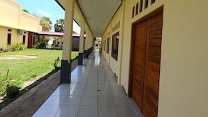 A corridor with tiled flooring, wooden doors, and a covered walkway with columns. - EduTel (Labuan Bajo)