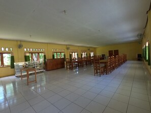 A spacious hall with tiled flooring, rows of wooden chairs, a reception desk, and windows with curtains. - EduTel (Labuan Bajo)