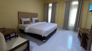 A hotel room with a large bed, a desk, a chair, and an air conditioning unit. - EduTel (Labuan Bajo)