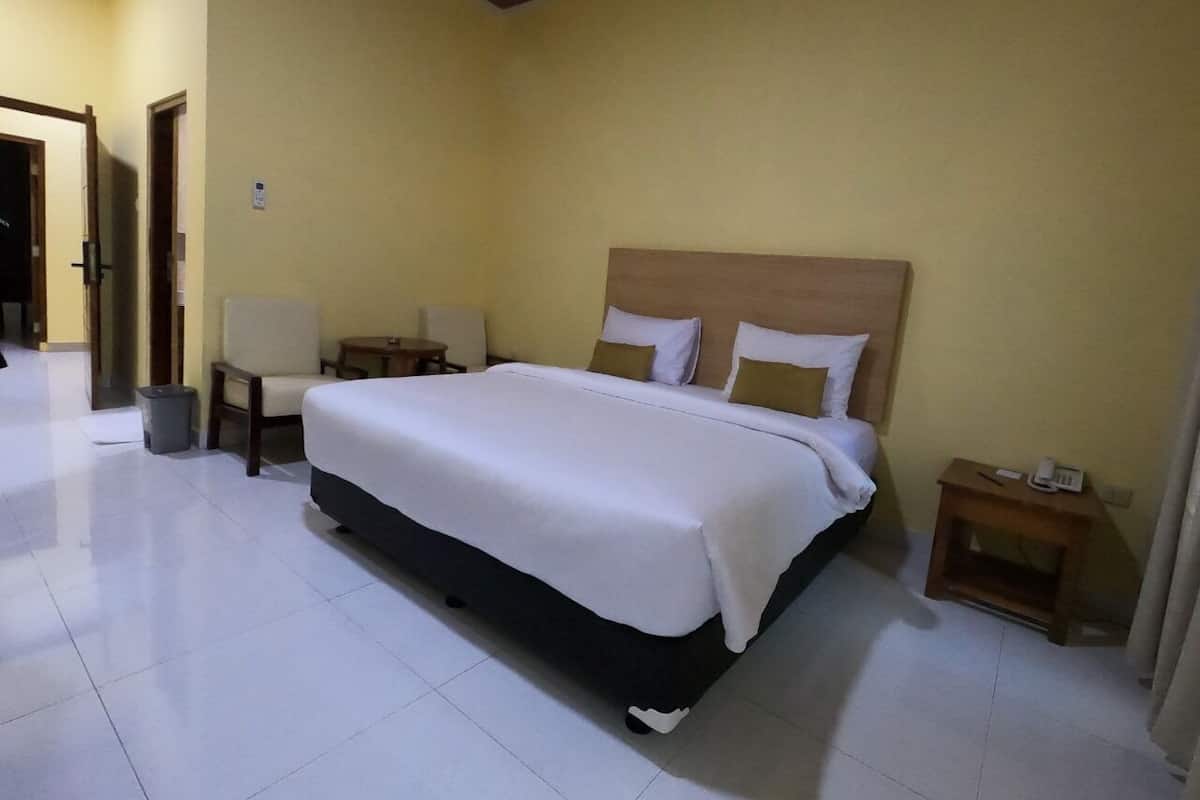 A hotel room with a large bed, bedside tables, a chair, and a trash bin.