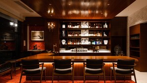 A bar area with a long wooden counter, four bar stools, and shelves stocked with bottles and glasses. - Abita Hotel Kyoto Kamogawa (Kyoto)