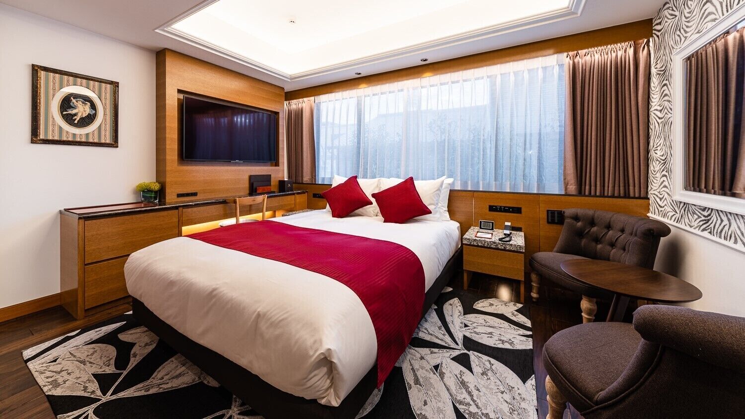 A hotel room with a bed, a TV, a desk, a chair, and a window with curtains.