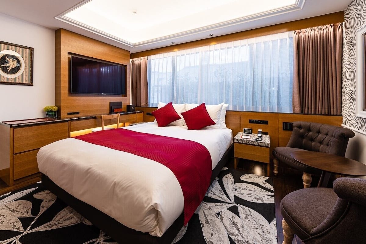 A hotel room with a bed, a TV, a desk, a chair, and a window with curtains.