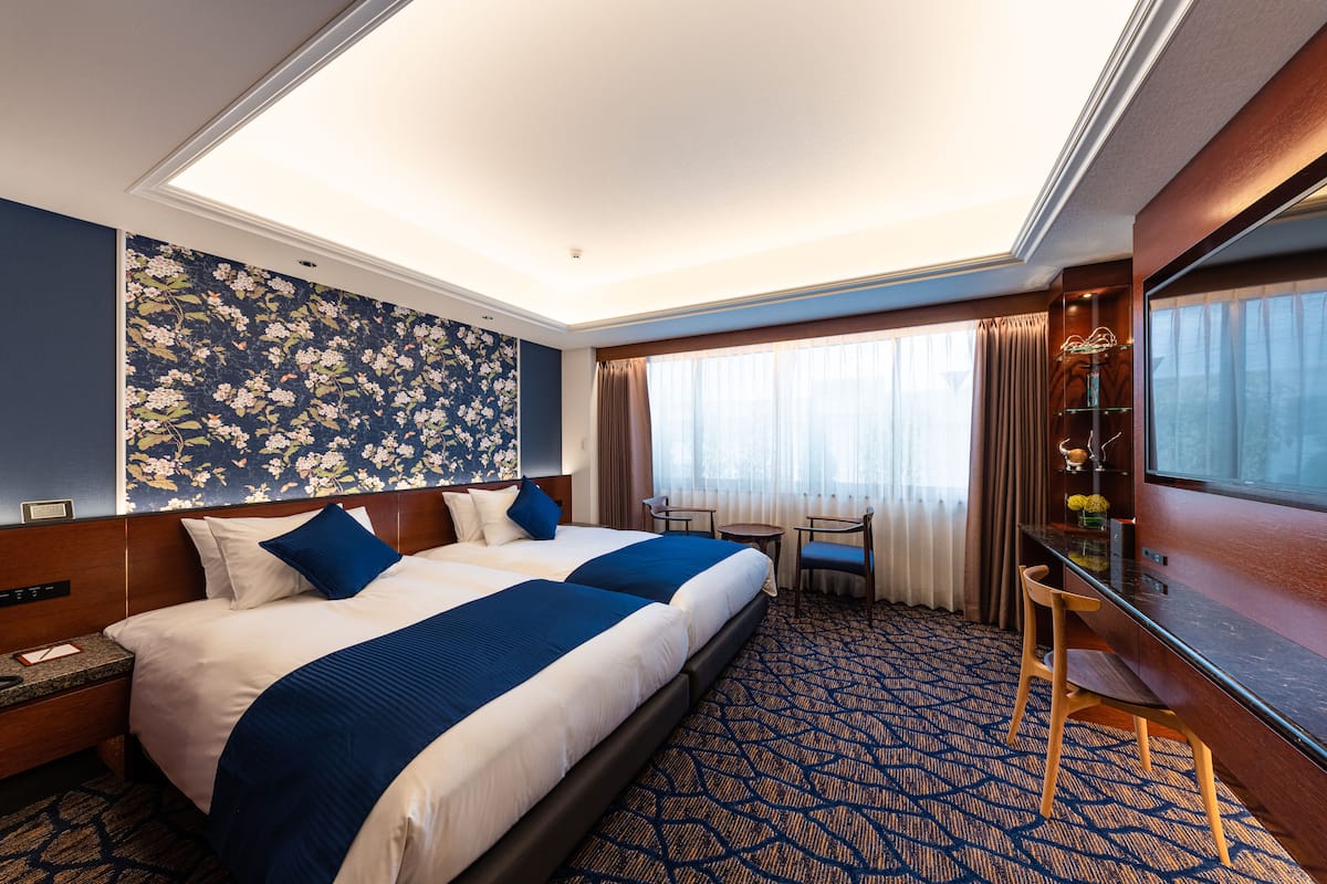 A hotel room with a large bed, a desk, a chair, and a window with curtains.