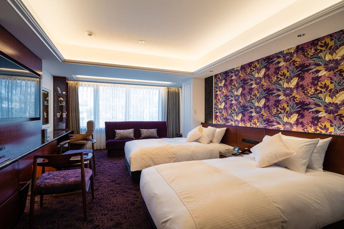 A hotel room with two beds, a desk, a chair, and a large floral wall.
