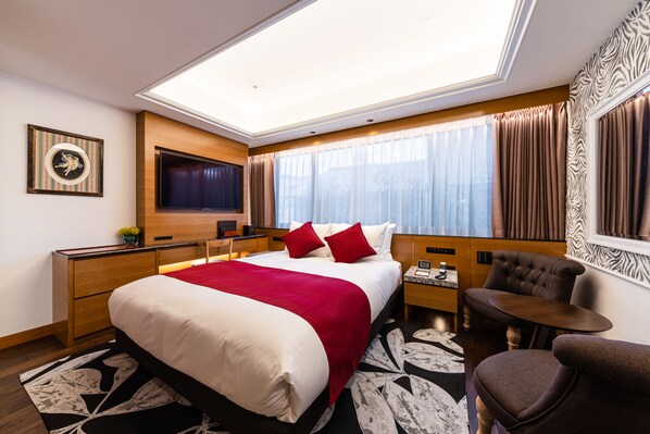 Quarto de hotel com uma cama grande, televisão de tela plana, escrivaninha com cadeira e janela com cortinas.