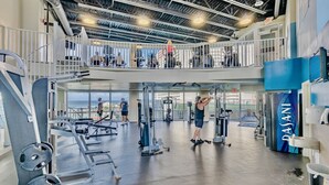 A multi-level gym with various exercise equipment, a balcony with a view, and a prominent logo on the wall.