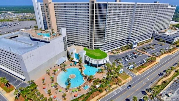 A large hotel with multiple floors, a central courtyard with a swimming pool, and a parking area.