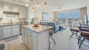 A modern kitchen with a large island, dining area with a round table and chairs, and a view of the outdoors through large windows.