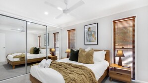 A modern bedroom with a large bed, bedside tables, a mirror, and wooden blinds.