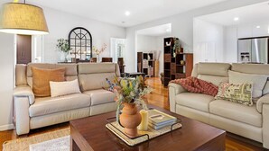 A spacious living room with two beige sofas, a coffee table with decorative items, and a large window with a view.