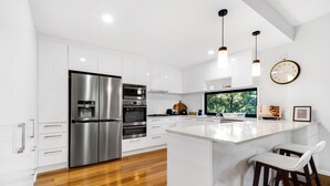 A modern kitchen with white cabinetry, stainless steel appliances, and a wooden island with bar stools.