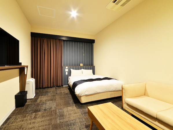 Habitación de hotel con cama, sofá, una mesita, televisión y ventana con cortinas.