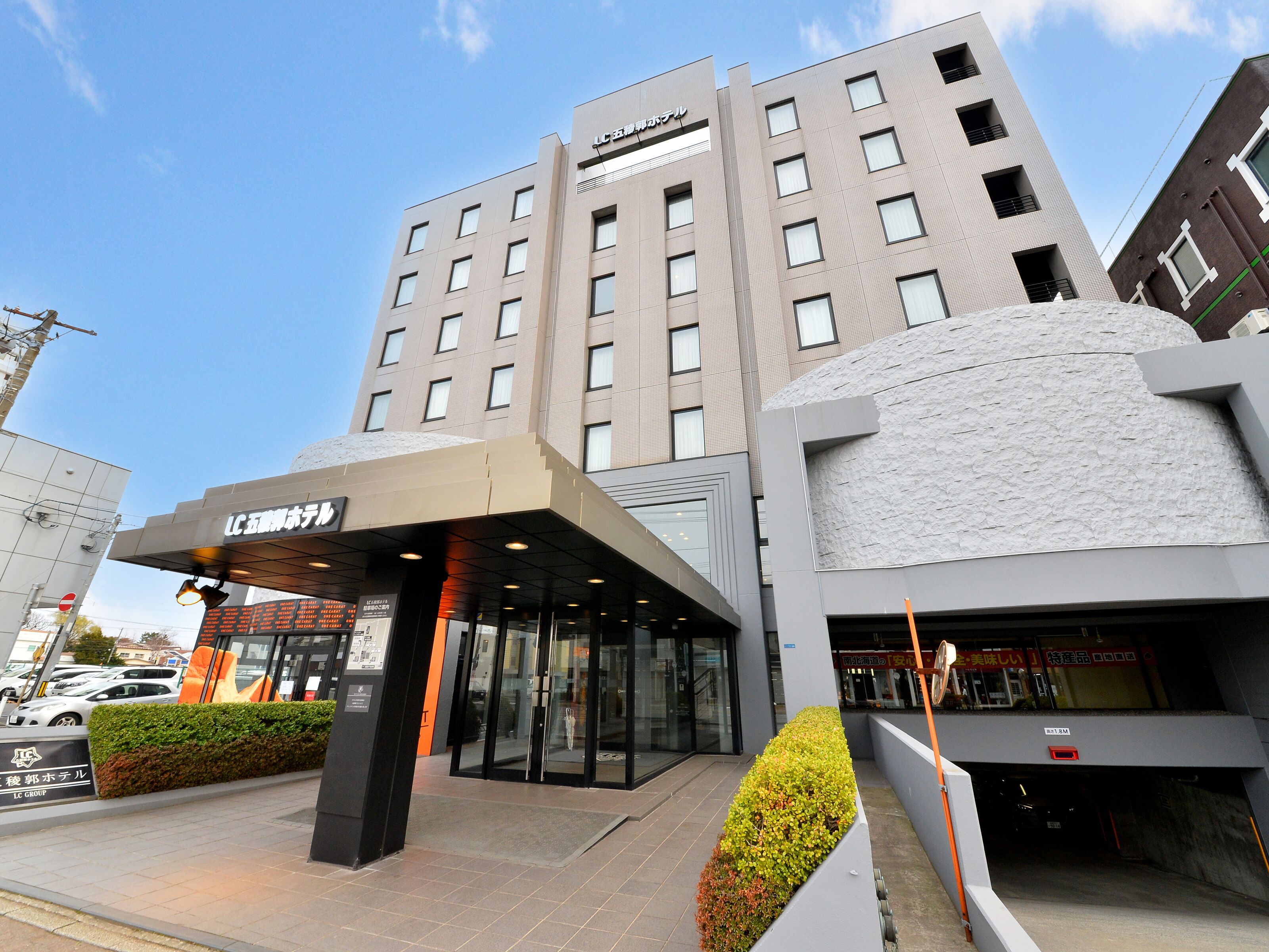 Een moderne hotelentree met een glazen gevel, een overdekt inkomgebied en een bord met de naam van het hotel.