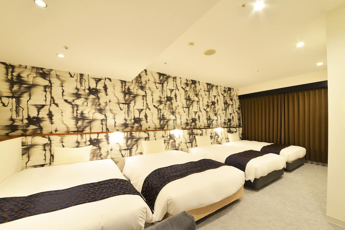 A hotel room with three beds, a patterned wall, and a large window with curtains.