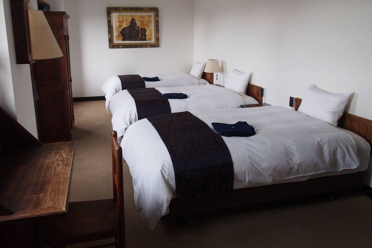A hotel room with three beds, a desk, and a painting on the wall.