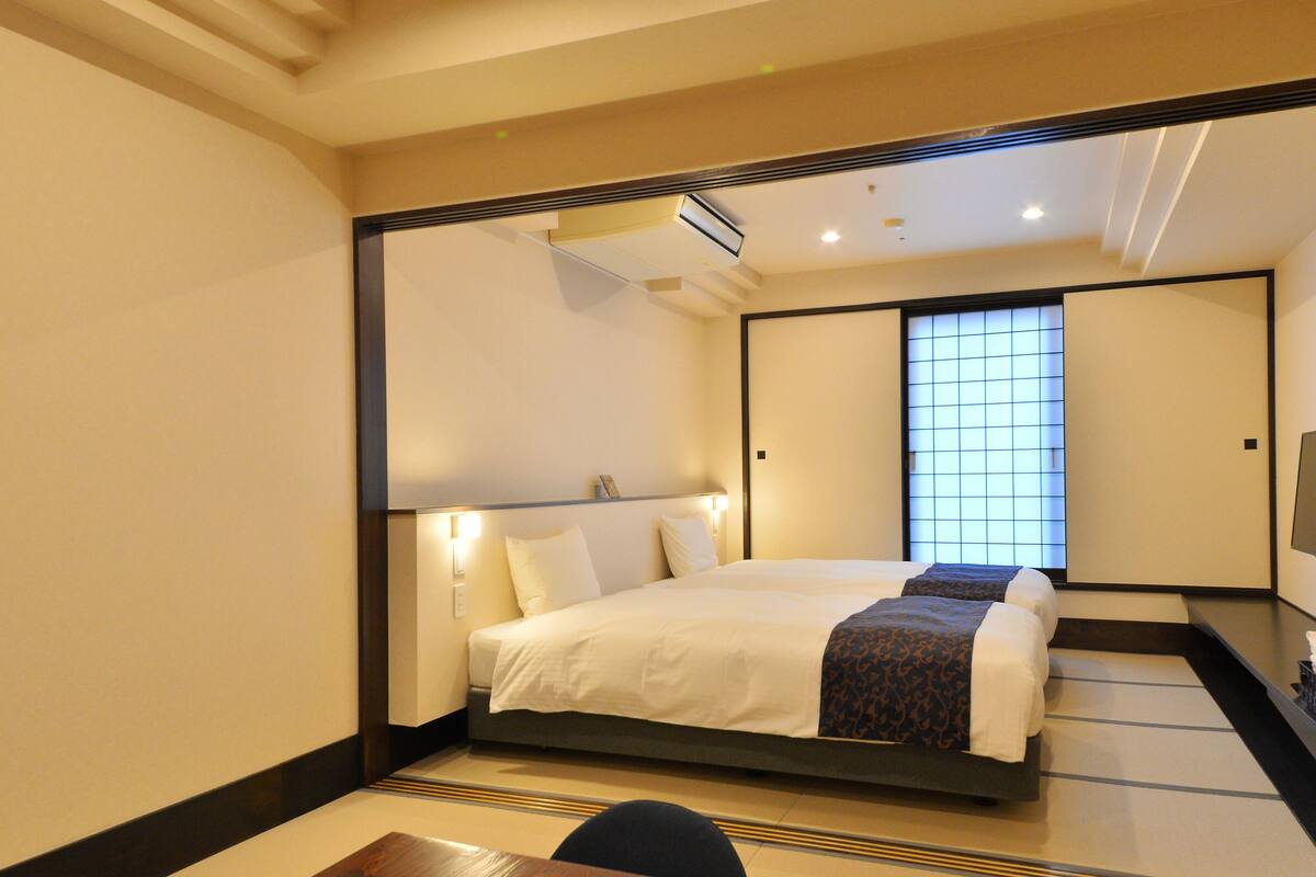 A hotel room with a large bed, a desk, and a sliding door leading to a balcony.