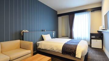 Habitación de hotel con cama, escritorio, silla, mesita, teléfono y espejo.