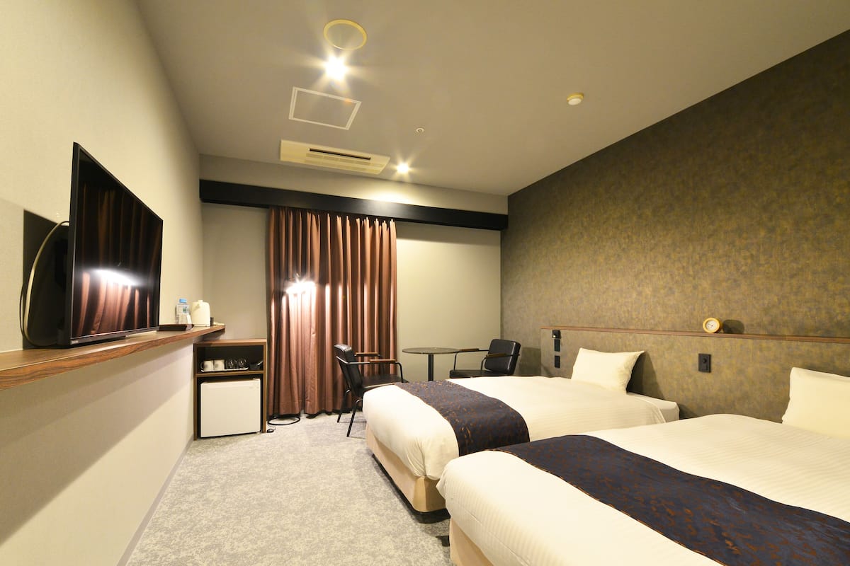A hotel room with two beds, a desk, a chair, a television, and a curtain.