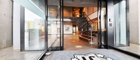 A hotel entrance with a glass door, a staircase leading to the upper floor, and a sign with Japanese characters.