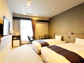 Ein Hotelzimmer mit zwei Betten, einem Schreibtisch, einem Stuhl, einem kleinen Tisch und einem Fernseher.