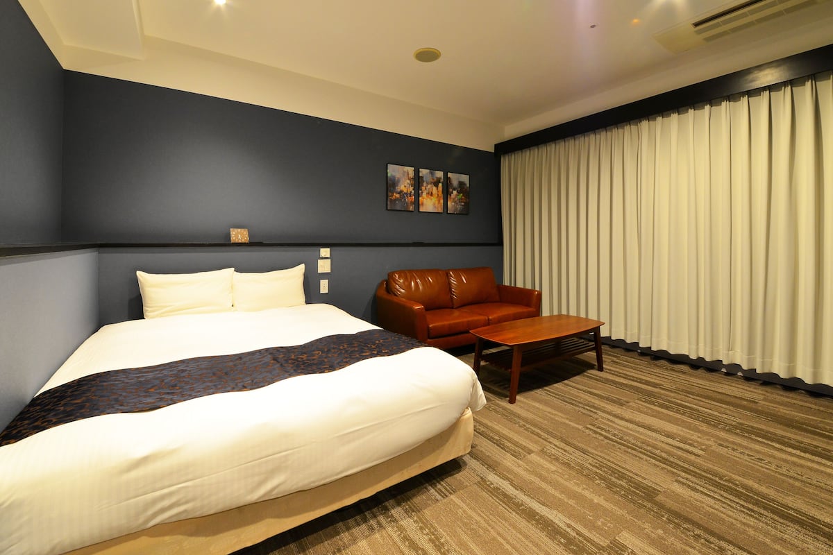 A hotel room with a large bed, a leather sofa, a small table, and a window with curtains.