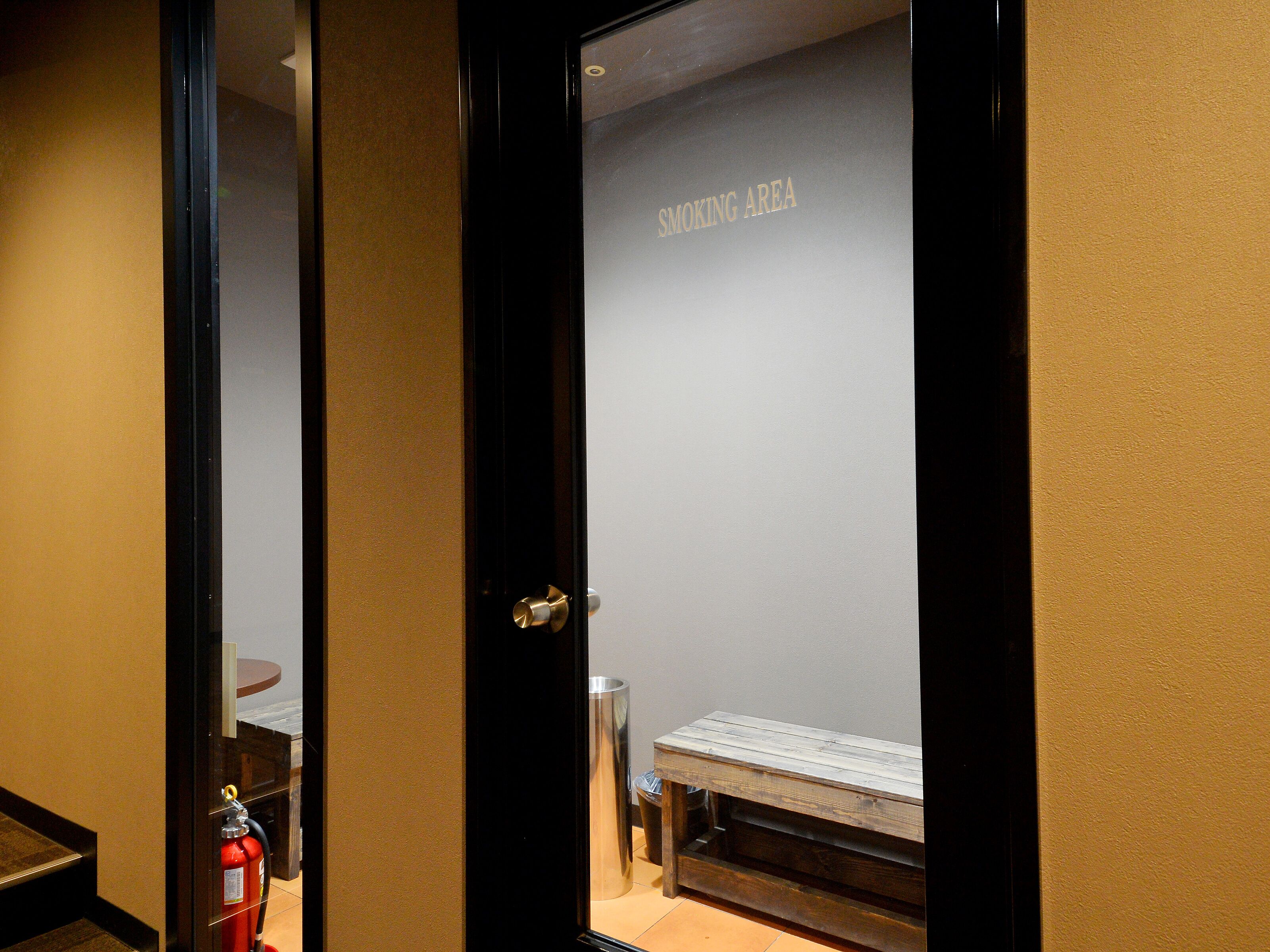 A hotel room with a wooden bench and a fire extinguisher near the door.
