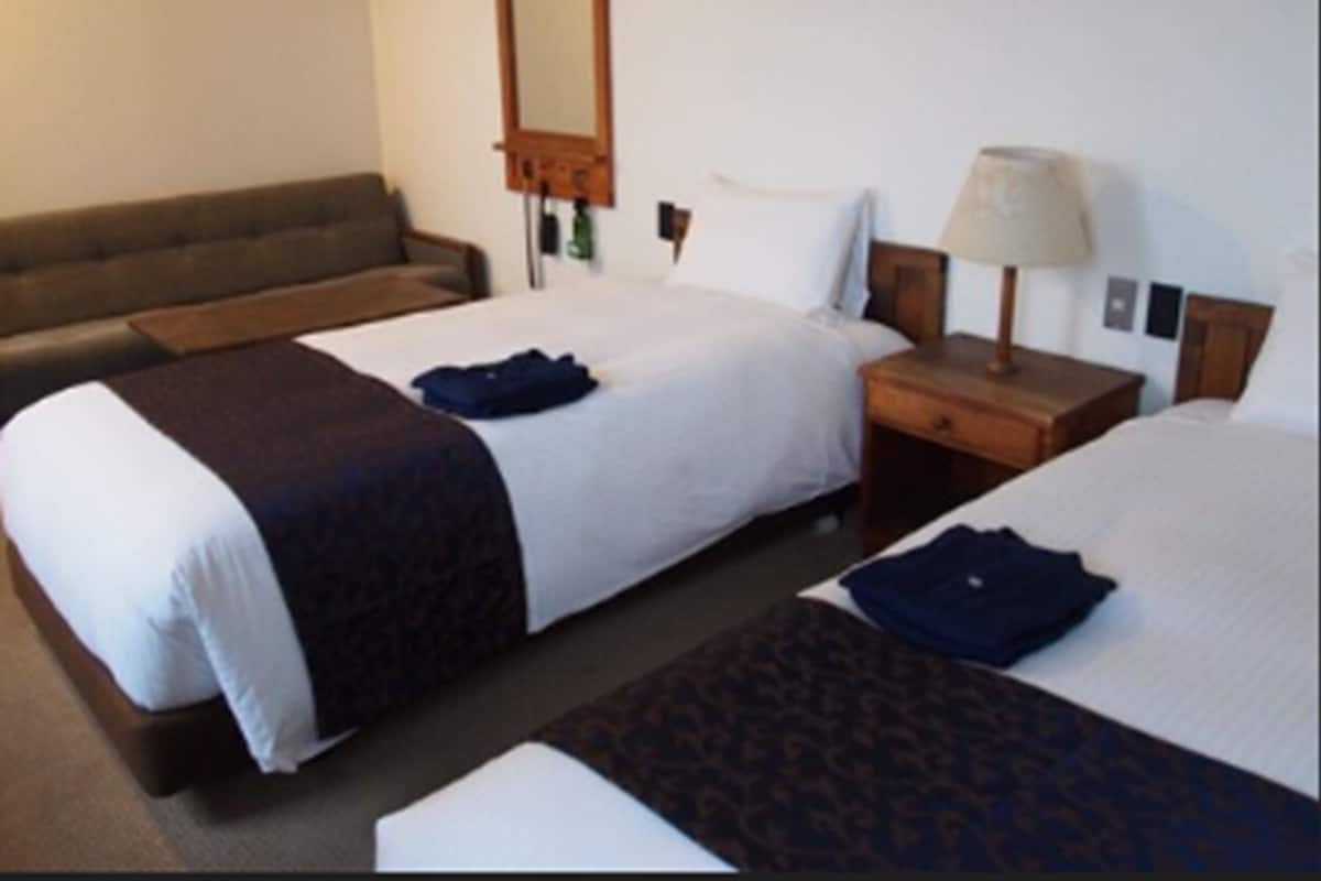 A hotel room with two beds, a sofa, a nightstand with a lamp, and a mirror on the wall.