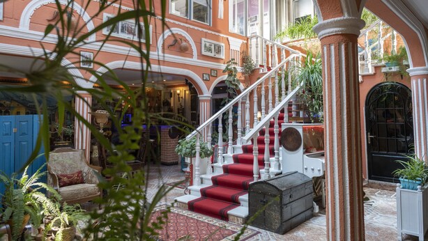 A grand staircase with red carpeted steps leading to an upper floor, surrounded by ornate architecture and potted plants. - Elia Boutique Hostel & Apart-Hotel (Tbilisi)