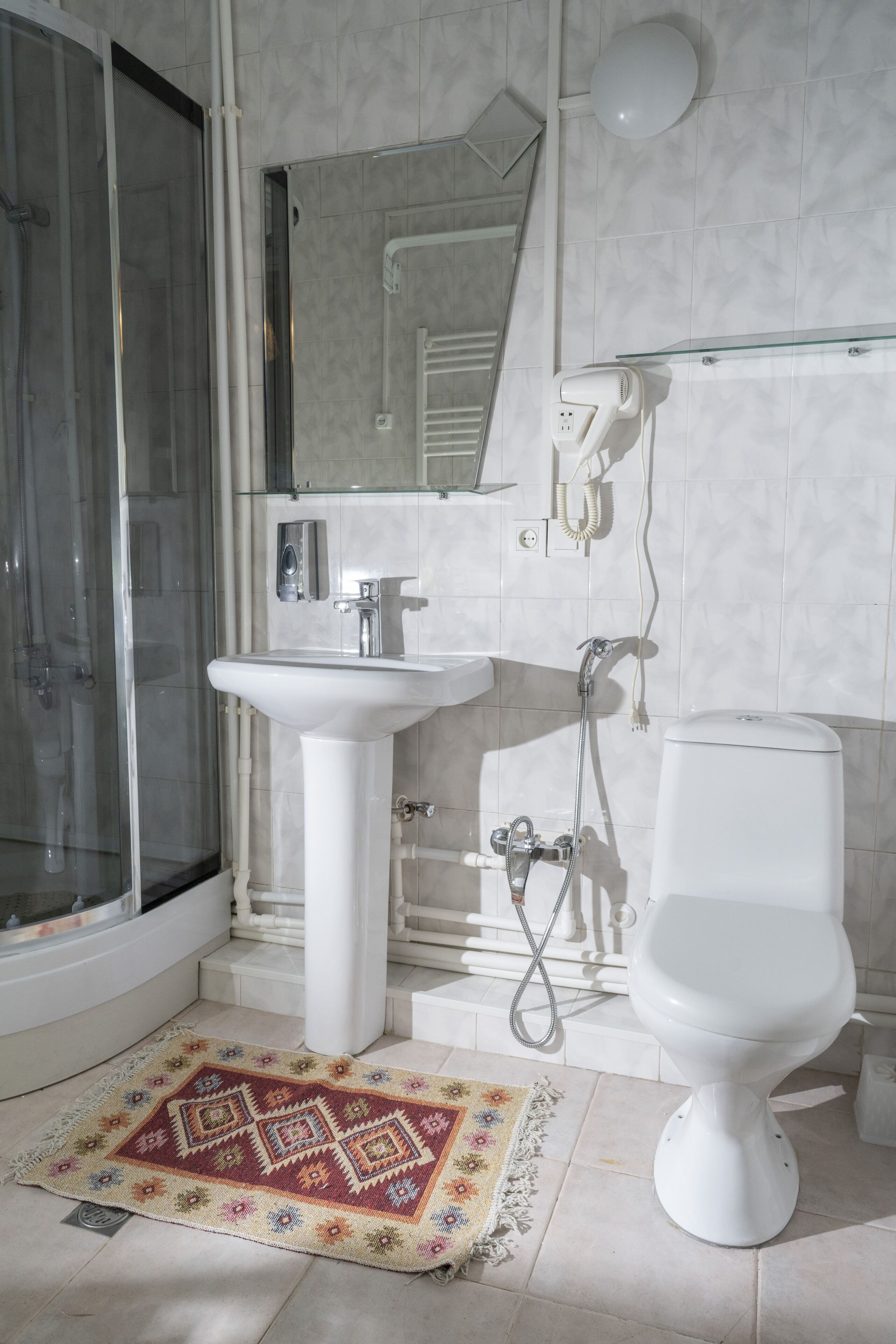 A bathroom with a glass shower enclosure, a white pedestal sink, a toilet, and a glass shelf above the sink.