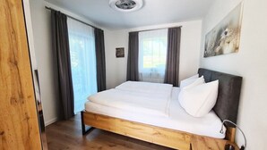 Ein modernes Schlafzimmer mit einem hölzernen Bettgestell, einem Nachttisch mit Lampe und einem großen Fenster mit Vorhängen.