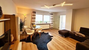 Ein modernes Wohnzimmer mit Holzboden, einem schwarzen Lederteppich, einer Essecke mit rundem Tisch und Stühlen, einer Couch und einem Fernseher.