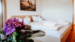 A neatly made bed with white linens and pillows, a framed picture on the wall, and a potted plant with purple flowers in the foreground. - Gasthaus Hirsch (Wangen im Allgäu)