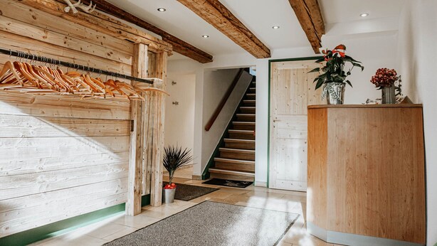 A wooden interior with a staircase, a reception desk, and a coat rack. - Gasthaus Hirsch (Wangen im Allgäu)