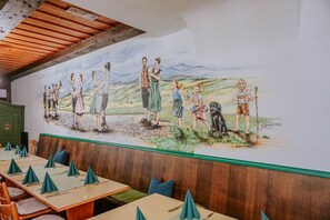 A restaurant with a mural depicting a rural scene, wooden ceiling beams, and neatly arranged tables with green napkins. - Gasthaus Hirsch (Wangen im Allgäu)