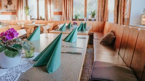 A restaurant with wooden tables and green napkins, cushioned benches, and potted plants. - Gasthaus Hirsch (Wangen im Allgäu)