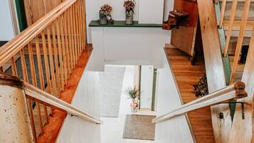 Un escalier en bois, avec une porte verte en haut, une petite table avec une plante et des lampes suspendues.