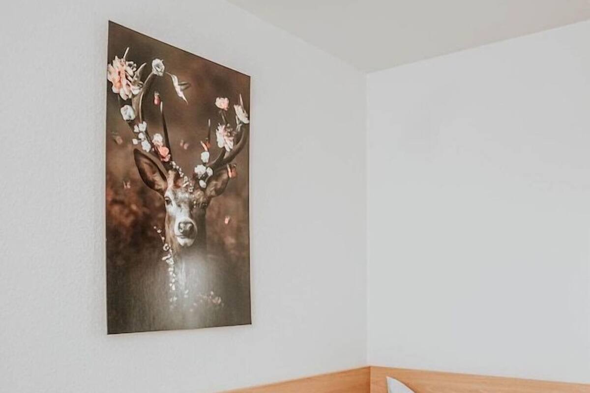 A single bed with a wooden headboard, a white pillow, and a wall-mounted painting of a deer with flowers.