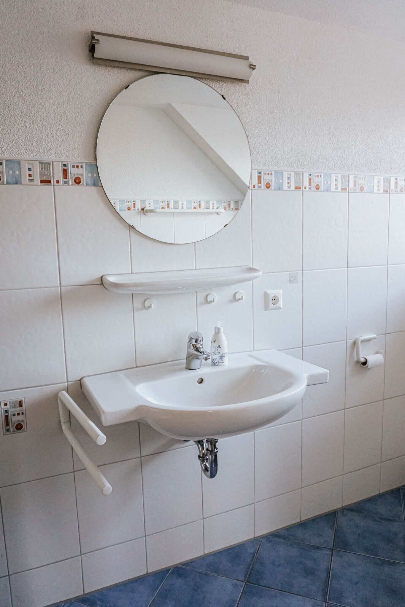 A bathroom with a white sink, a round mirror, and a shelf above the sink.