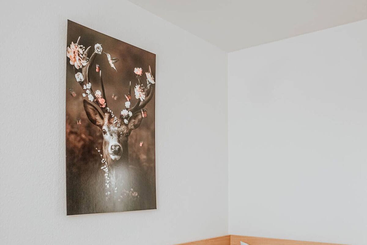 A single bed with a wooden headboard, white bedding, and a wall-mounted painting of a deer with flowers.